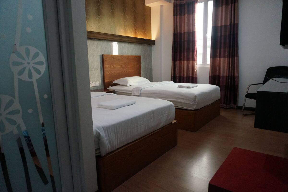 Habitación de hotel con dos camas, cabecera de madera, ventana con cortinas, escritorio y alfombra roja.