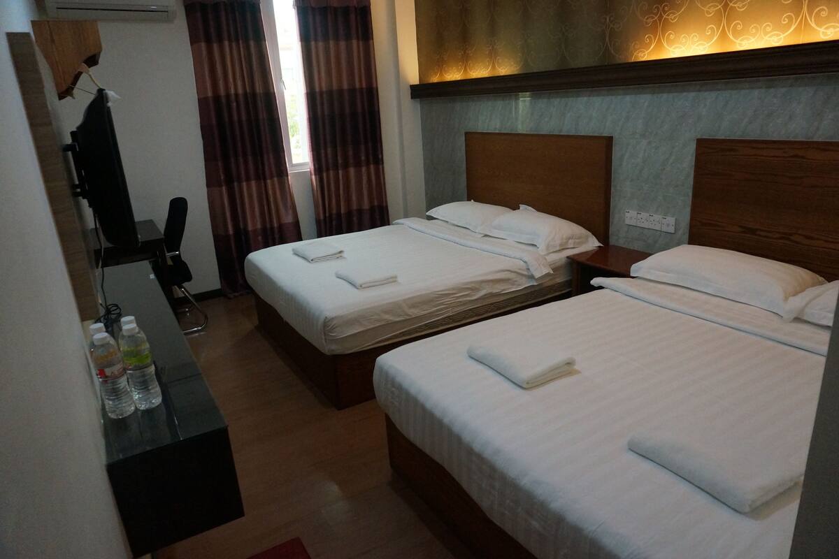 Una habitación de hotel con dos camas, un escritorio con una silla y un armario.