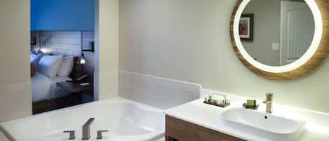 A modern bathroom with a large bathtub, a sink, and a mirror with a wooden frame.