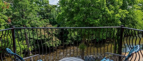 Een balkon met twee blauwe stoelen en een kleine ronde tafel, met uitzicht op een rivier en weelderige begroeiing.