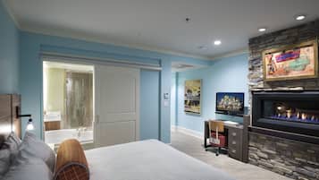 A bedroom with a bed, a desk, a fireplace, and a bathroom visible through an open door.