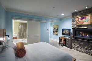 A bedroom with a bed, a desk, a fireplace, and a bathroom visible through an open door.
