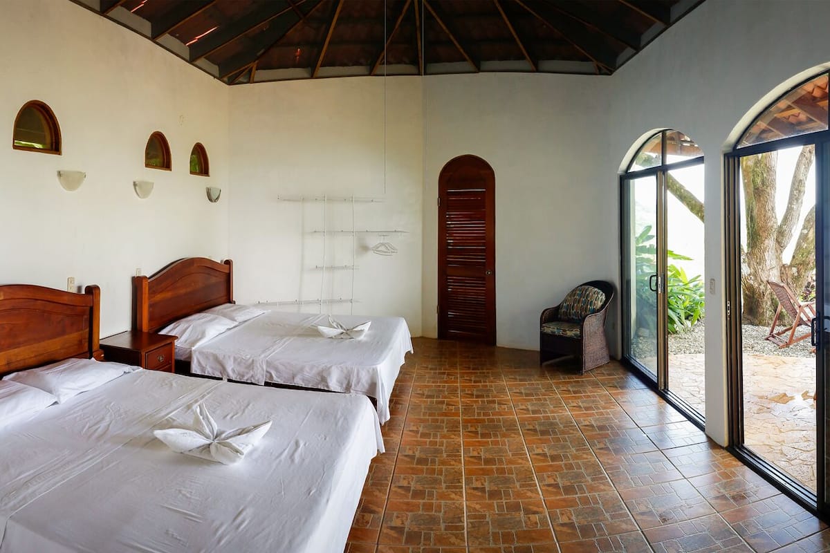 A hotel room with two wooden beds, a small seating area, and a large sliding glass door leading to an outdoor patio.