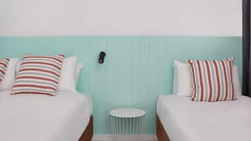 A hotel room with two beds, each with striped pillows, a small round side table, and a wall-mounted phone.
