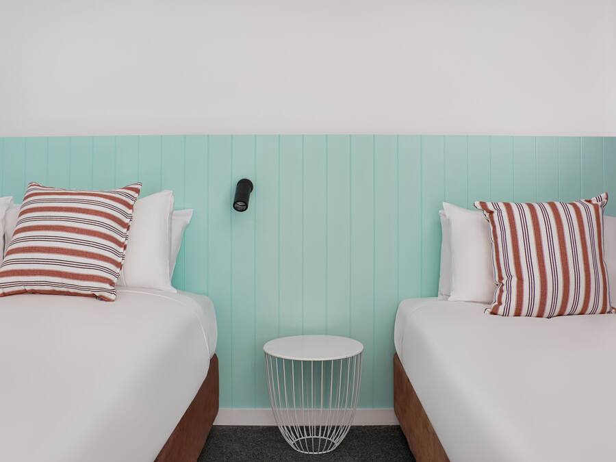 A hotel room with two beds, each with striped pillows, a small round side table, and a wall-mounted phone.