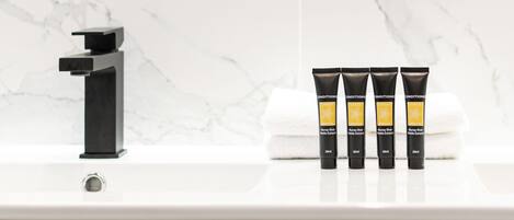 Un baño con un grifo negro, una pared de mármol y cuatro tubos de crema Muray River White Essence sobre un lavamanos blanco.