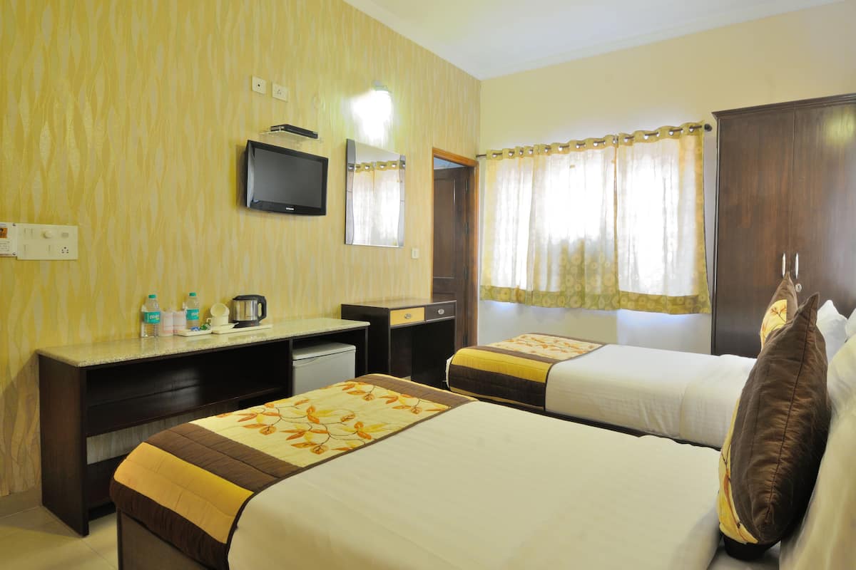 A hotel room with two beds, a desk, a television, and a window with curtains.