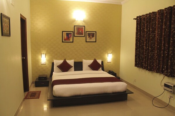 A hotel room with a large bed, two bedside tables, a wall-mounted TV, and a power outlet. - Hotel Persona International (New Delhi)