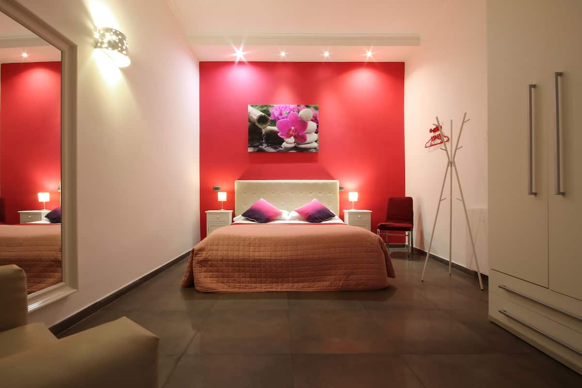 A modern bedroom with a large bed, a red accent wall, and a decorative wall art piece.