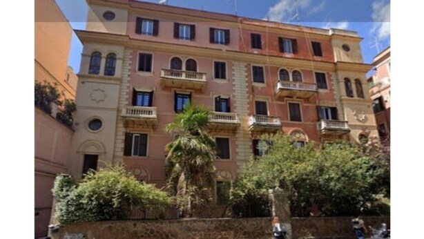 Un edificio de varios pisos con balcones y un muro de piedra en primer plano.