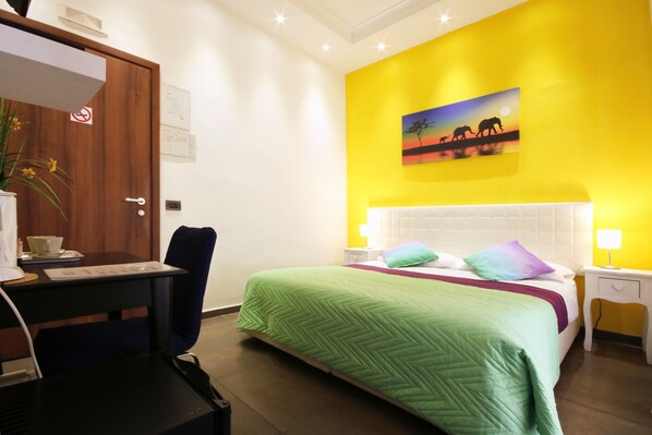 A hotel room with a bed, a desk, a chair, a nightstand, and a wall with a painting.