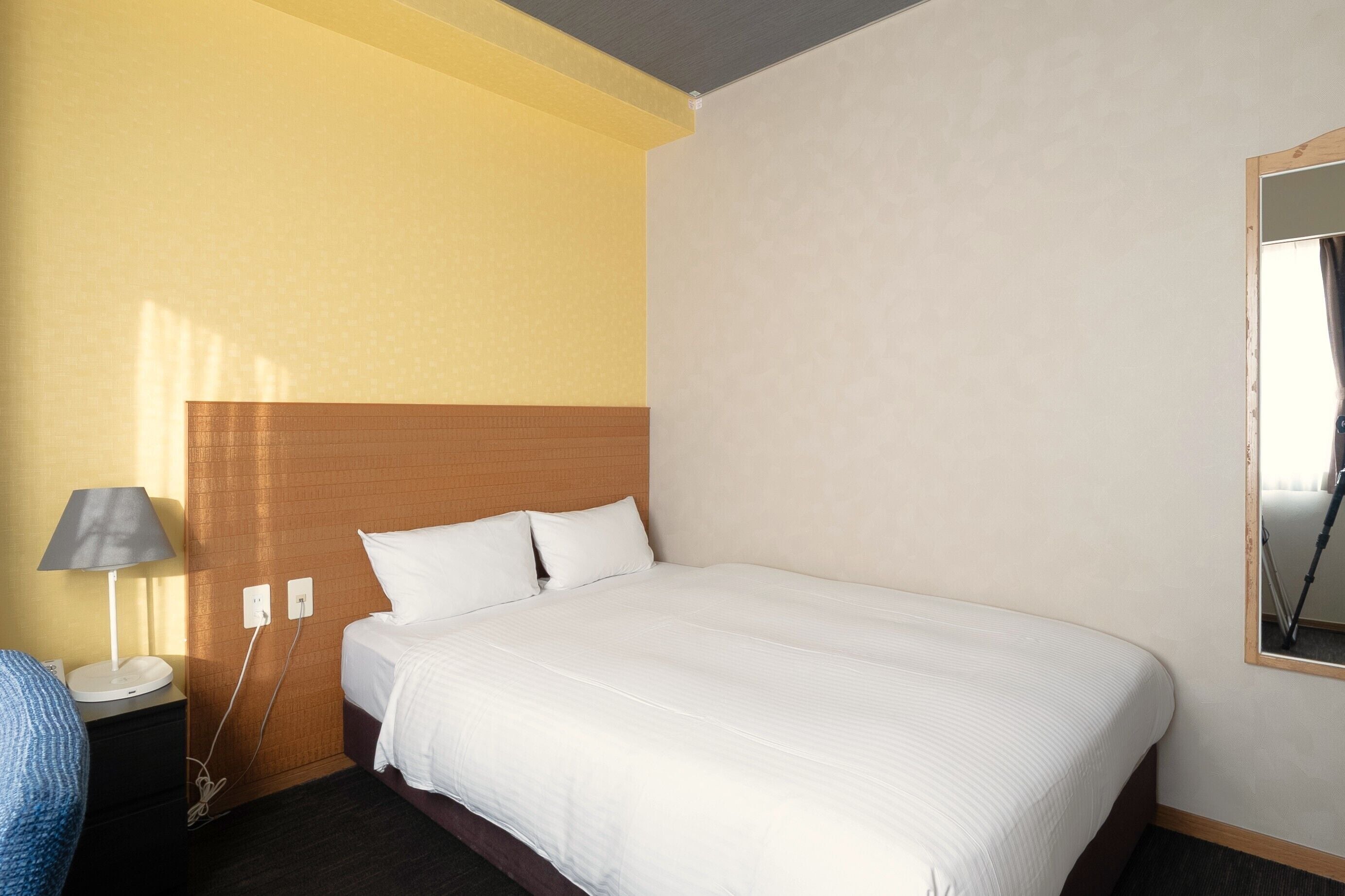 A hotel room with a large bed, a bedside lamp, and a mirror on the wall.