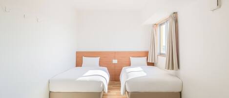 A room with two beds, a wooden headboard, a window with curtains, and an air conditioning unit.