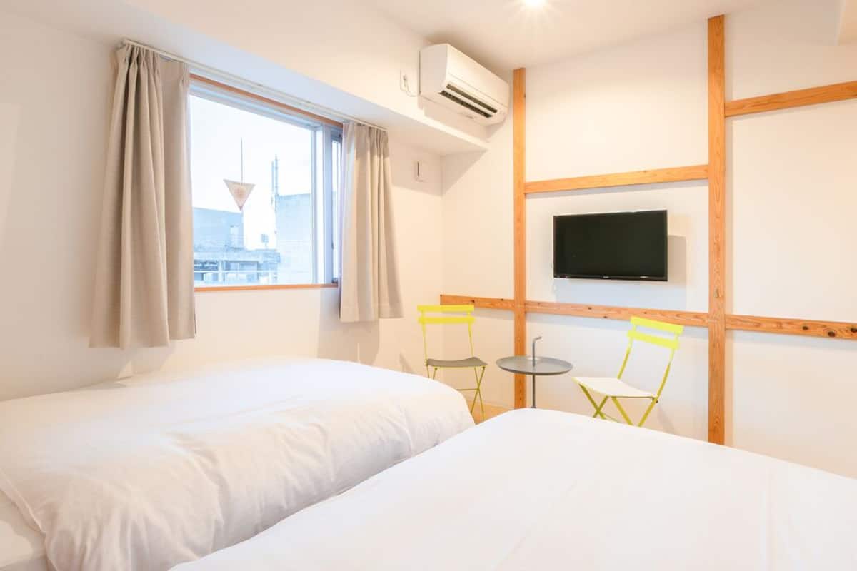 Une chambre d’hôtel avec deux lits, une télévision, un appareil de climatisation et une fenêtre avec des rideaux.