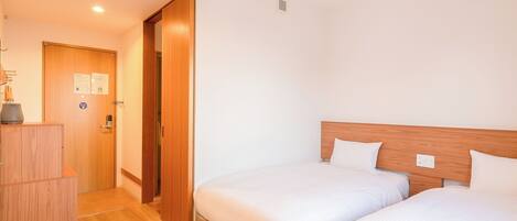 A hotel room with two beds, wooden headboards, a wooden wardrobe, and a door with a notice.