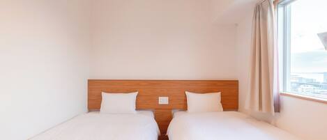 Une chambre d’hôtel avec deux lits simples, une tête de lit en bois, une fenêtre avec des rideaux et une vue sur la ville.