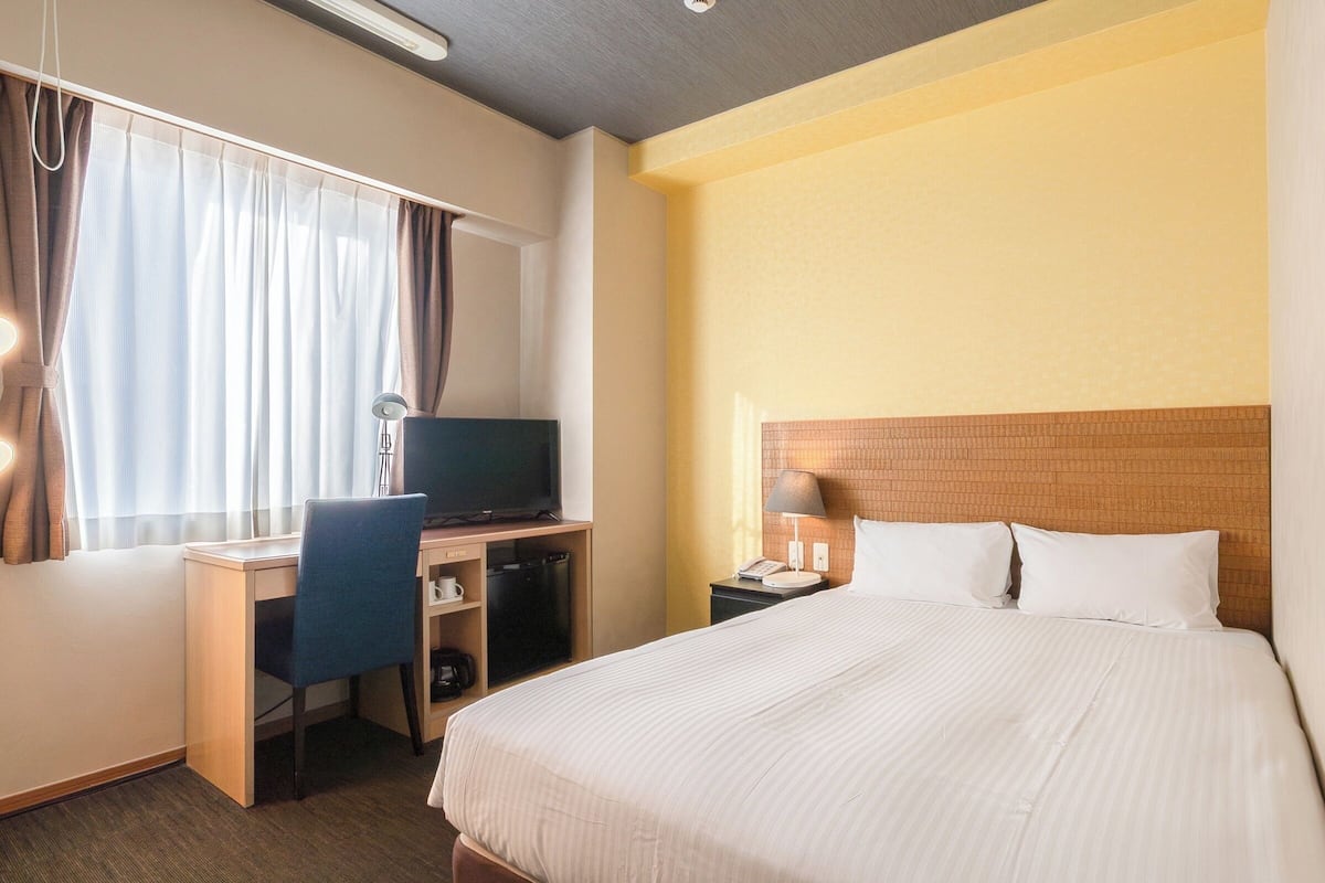 Une chambre d’hôtel équipée d’un lit, d’un bureau, d’une chaise, d’une télévision et d’une table de chevet avec une lampe.