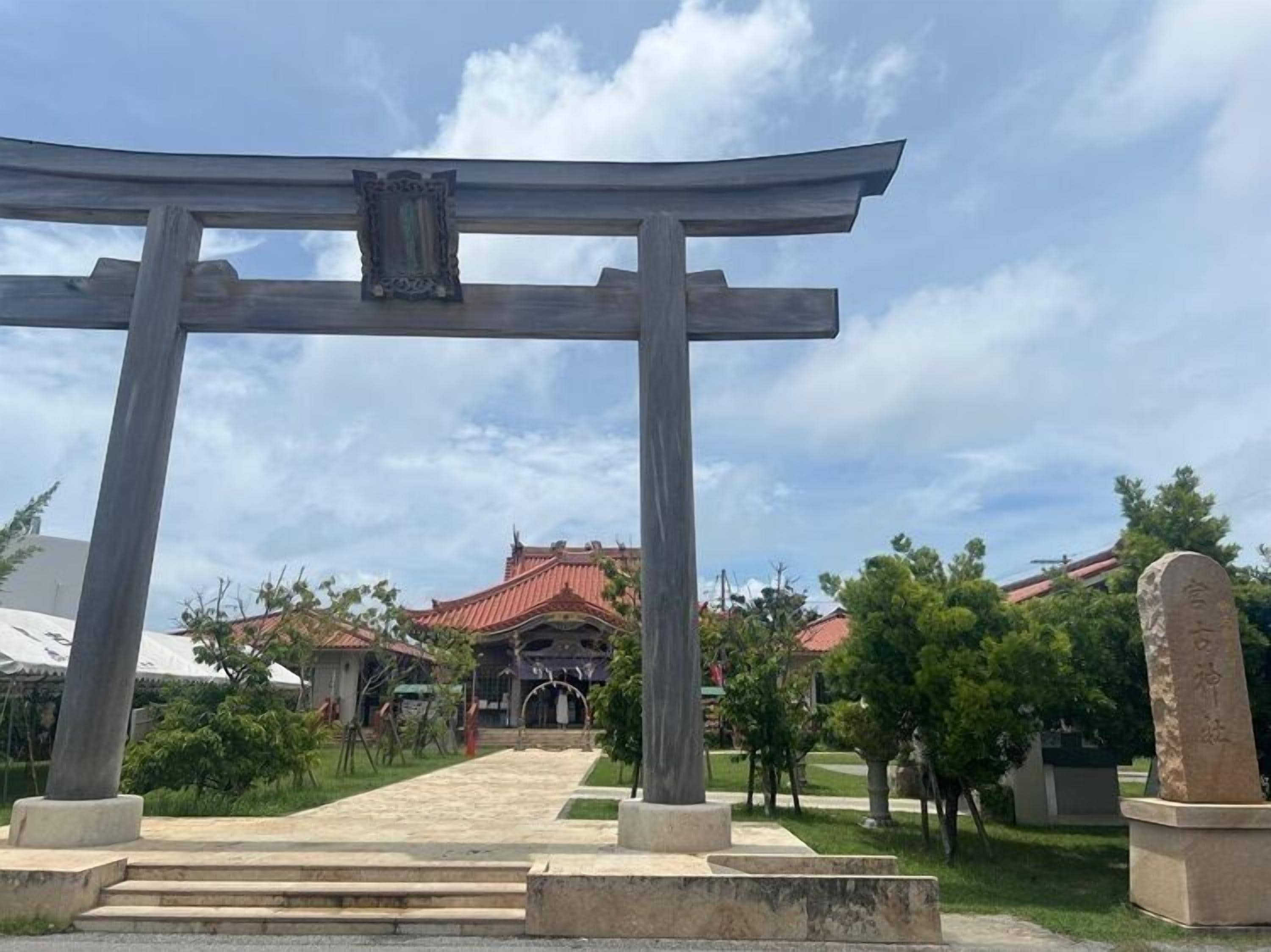 Un torii japonés tradicional con un monumento de piedra a su lado, que conduce a un edificio de techo rojo.