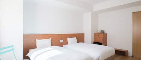 A modern hotel room with two beds, a wooden headboard, a small bedside table, and a chair.