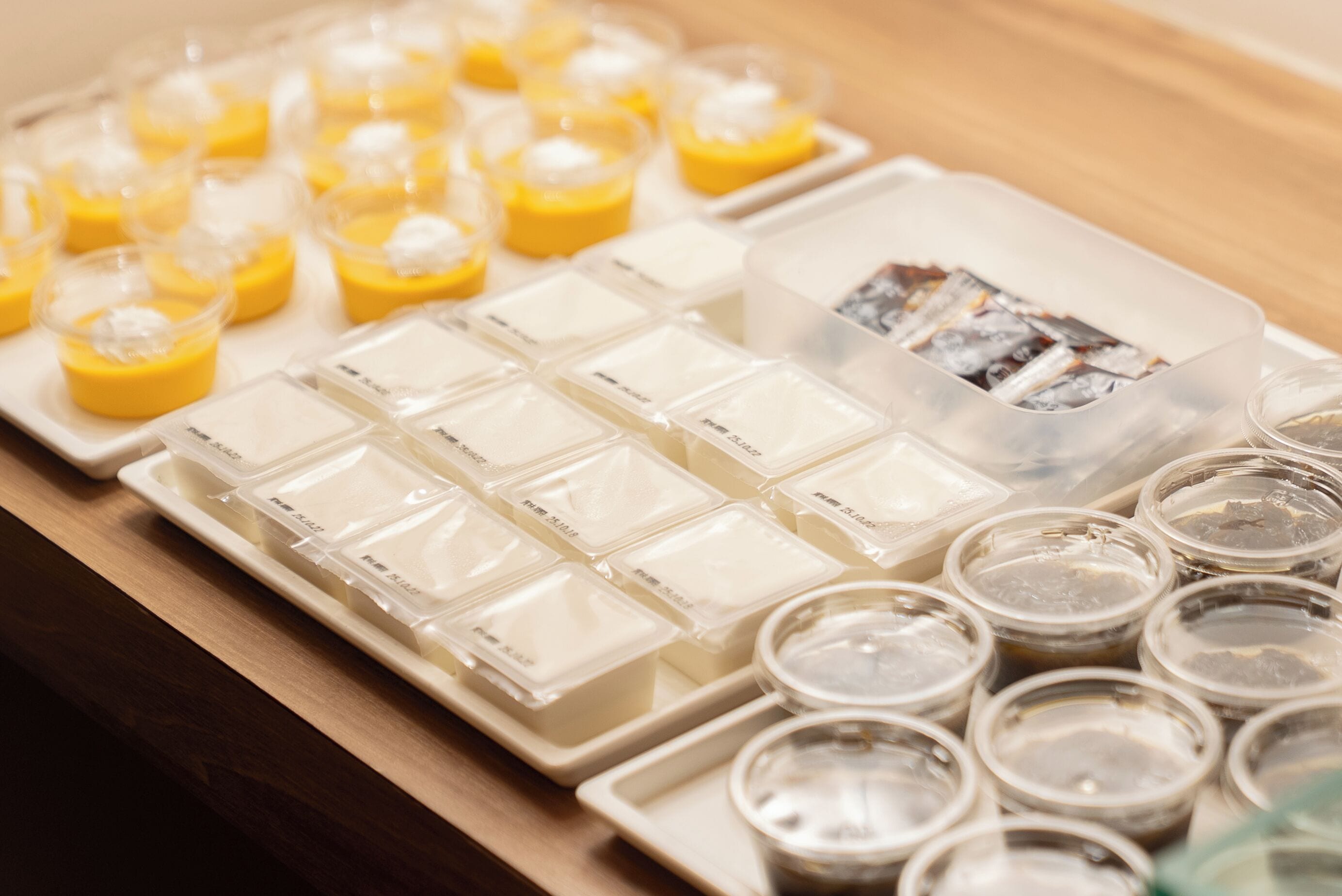 Una bandeja con diversos alimentos, incluyendo pequeñas copas de postre amarillo y varios recipientes con sustancias blancas y marrones.