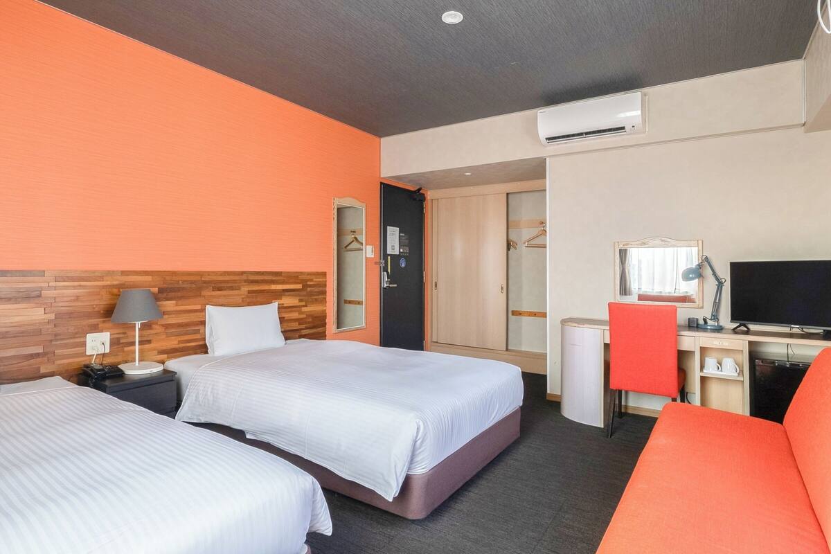 Une chambre d’hôtel avec deux lits, un bureau, une chaise, une télévision et une armoire.
