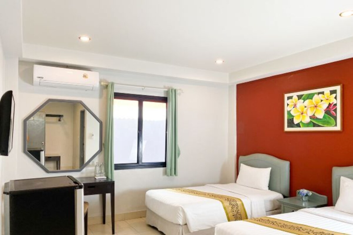 A hotel room with two beds, a desk, a mirror, an air conditioning unit, and a window with curtains.