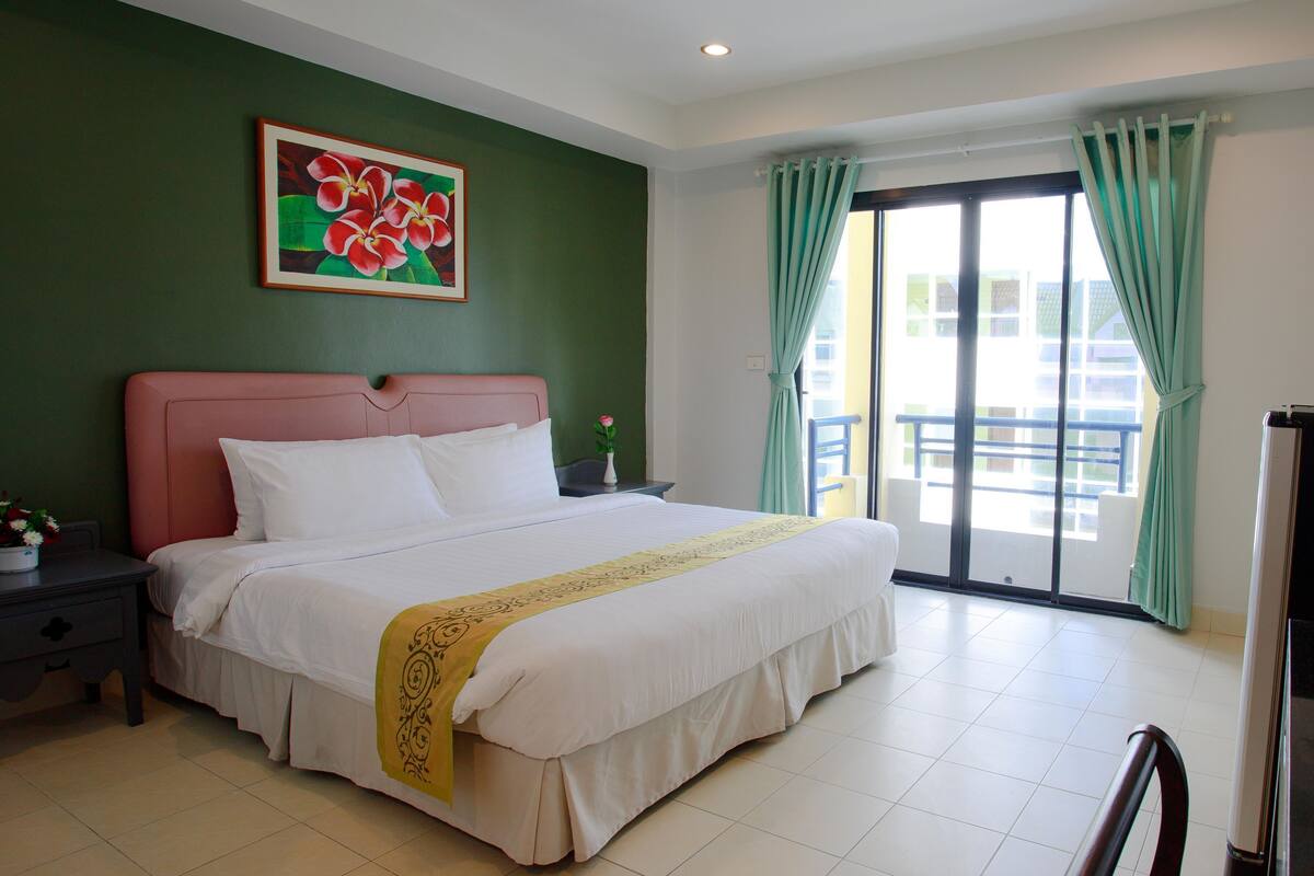 Habitación de hotel con una cama grande, una mesita de noche, un cuadro de flores y vistas al exterior a través de una puerta corrediza.