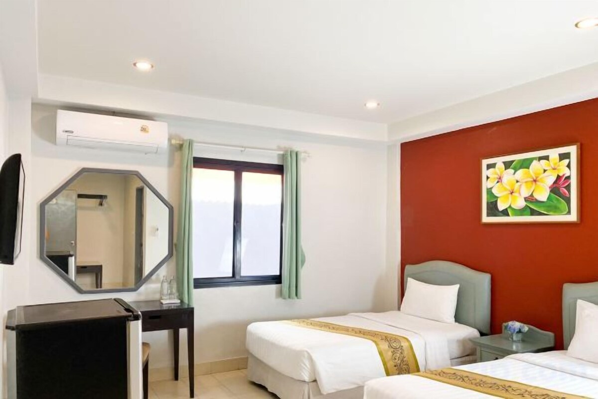A hotel room with two beds, a desk, a mirror, and a window with curtains.