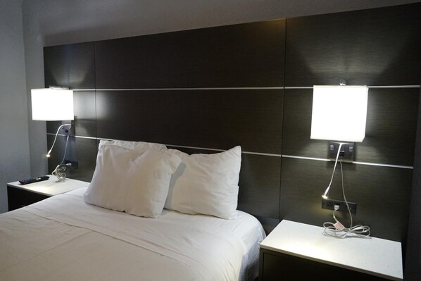 A hotel room with a large bed, two bedside tables, and two wall-mounted lamps.