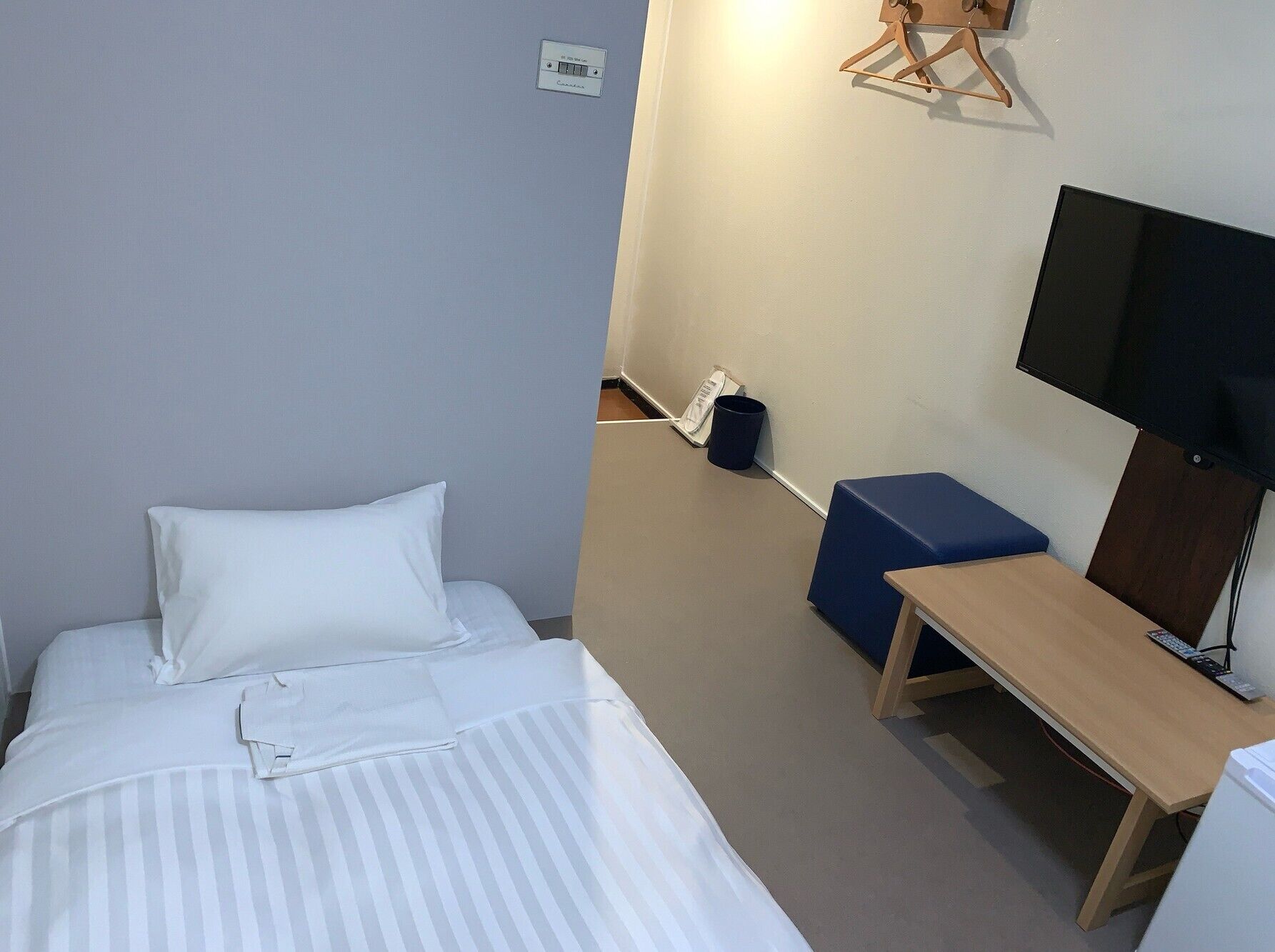 A hotel room with a bed, a desk, a chair, a television, and a wall-mounted light fixture.