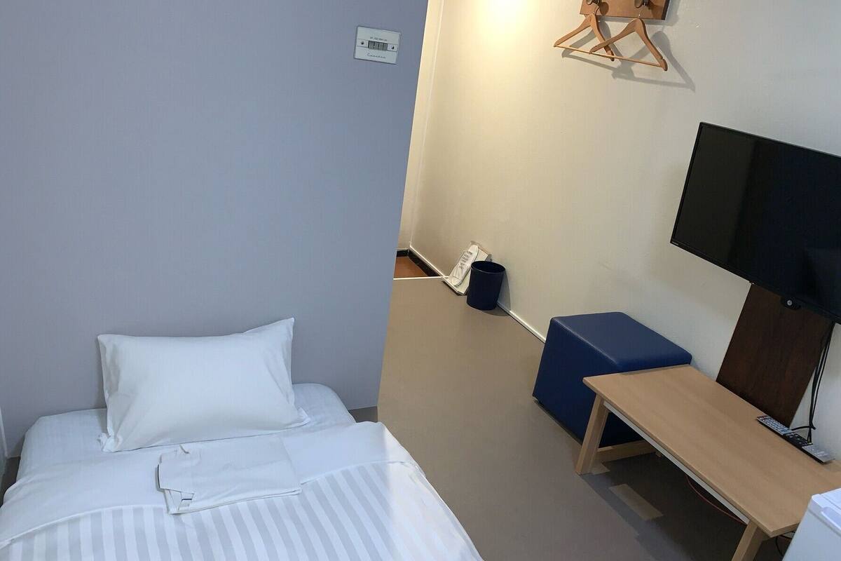 A hotel room with a bed, a desk, a chair, a television, and a wall-mounted light fixture.