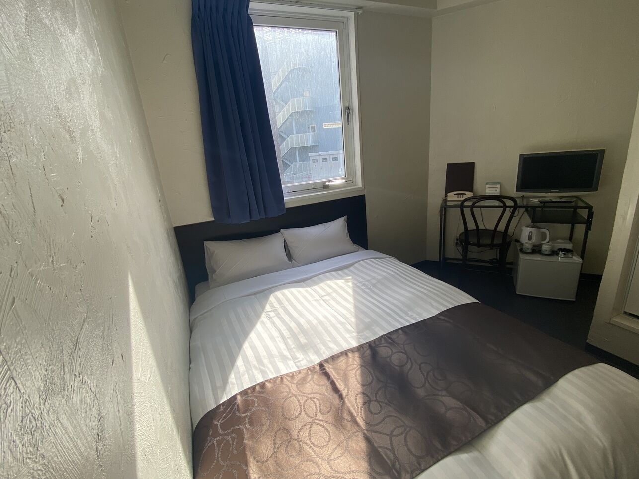 A hotel room with a bed, a television, a coffee maker, and a window with curtains.