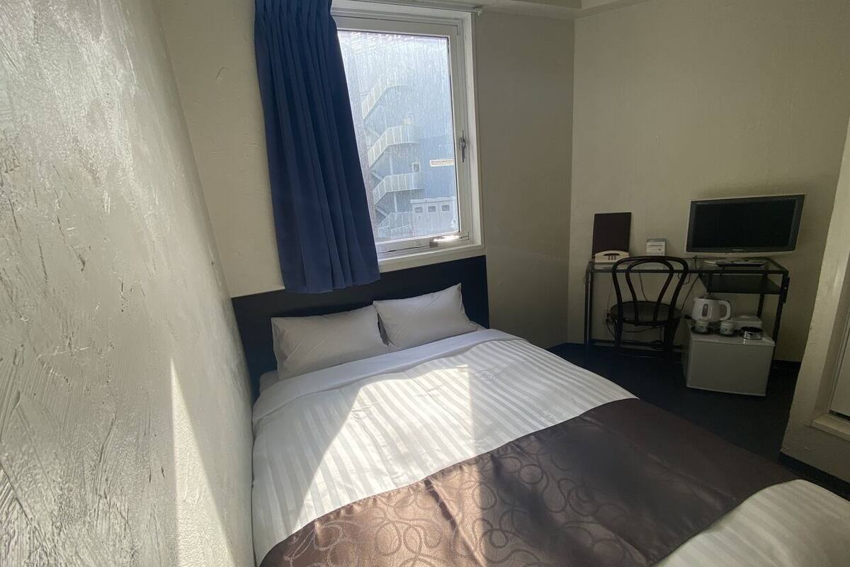 A hotel room with a bed, a television, a coffee maker, and a window with curtains.