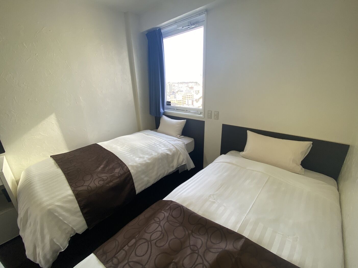 A hotel room with two beds, a window with a view, and a plain wall.
