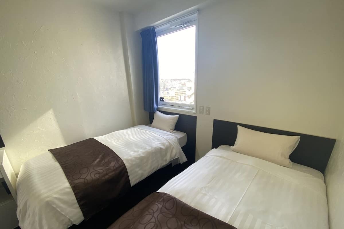 A hotel room with two beds, a window with a view, and a plain wall.