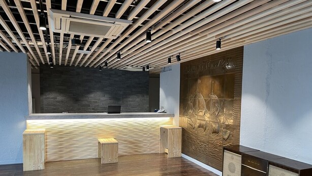A modern reception area with a wooden reception desk, a textured wall, and a ceiling with exposed beams and lighting fixtures. - Hotel Mayflower Sendai (Sendai)