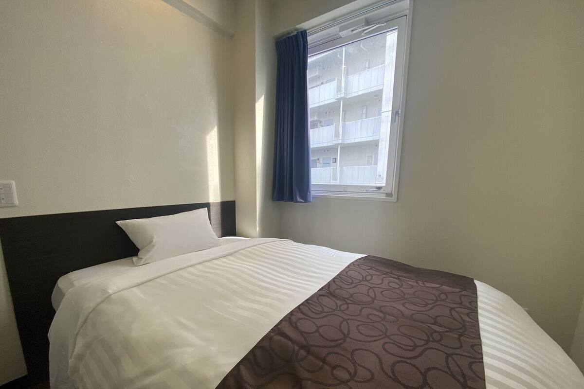 Une chambre d’hôtel avec un lit, une fenêtre avec des rideaux et une vue sur les bâtiments environnants.