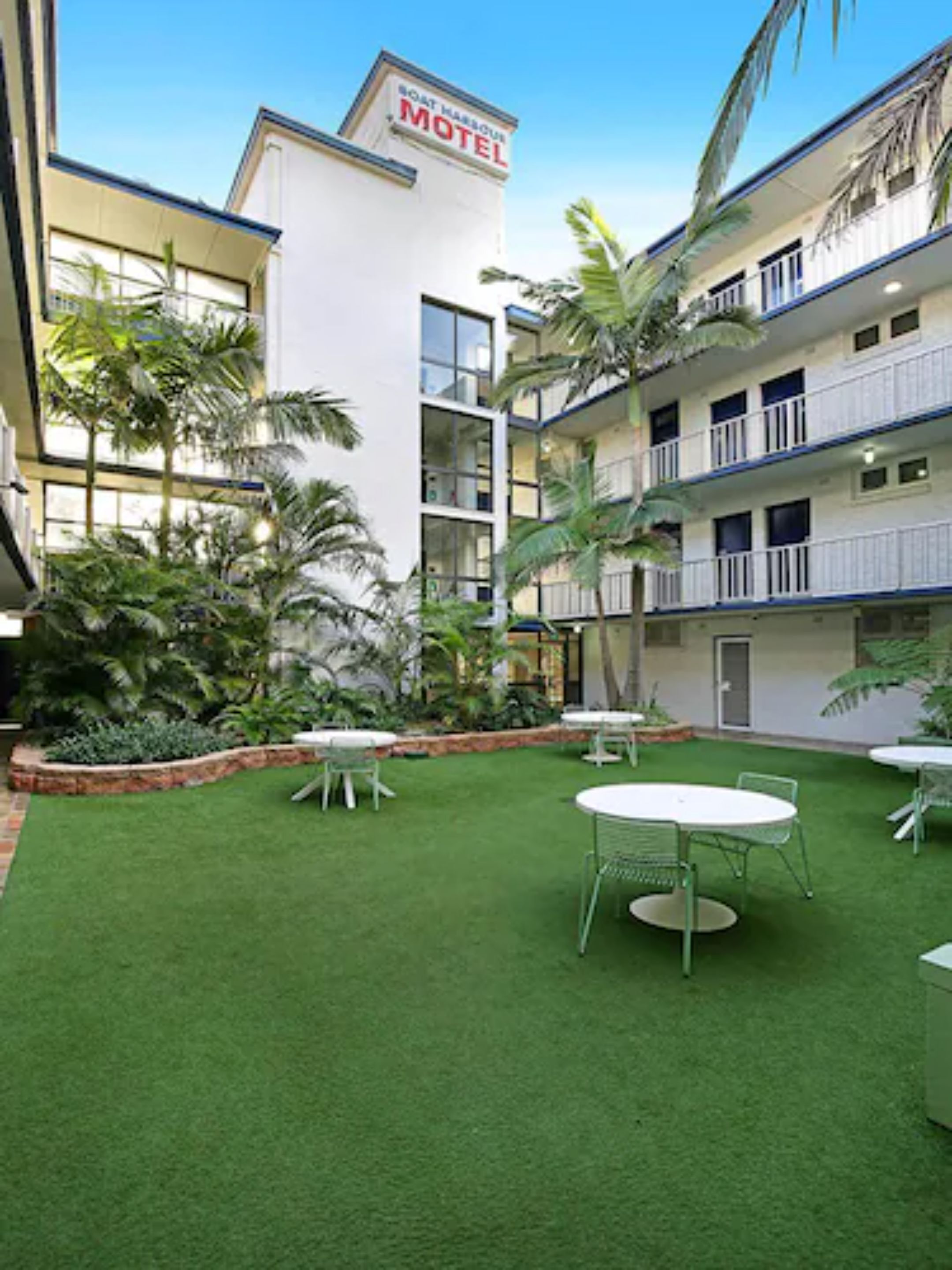 A motel with a sign indicating its name, a courtyard with artificial grass, and several tables and chairs.
