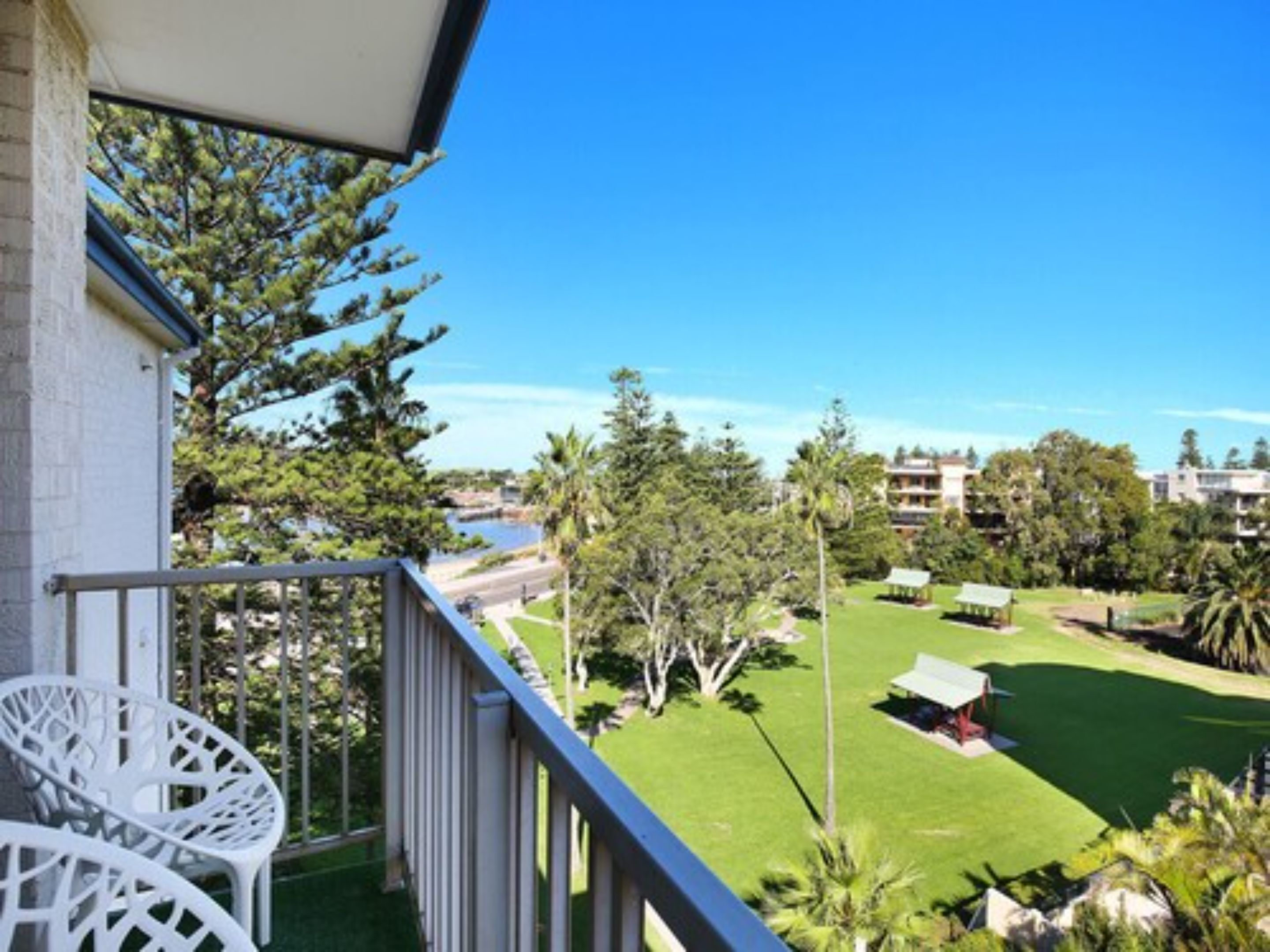 A balcony with white chairs, a view of a golf course, and a building in the background.