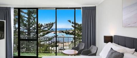 A modern hotel room with a large bed, a small table, and a view of a pool and trees.