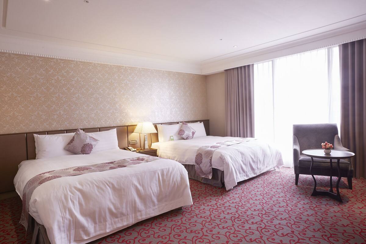 A hotel room with two beds, a small table, and a chair.