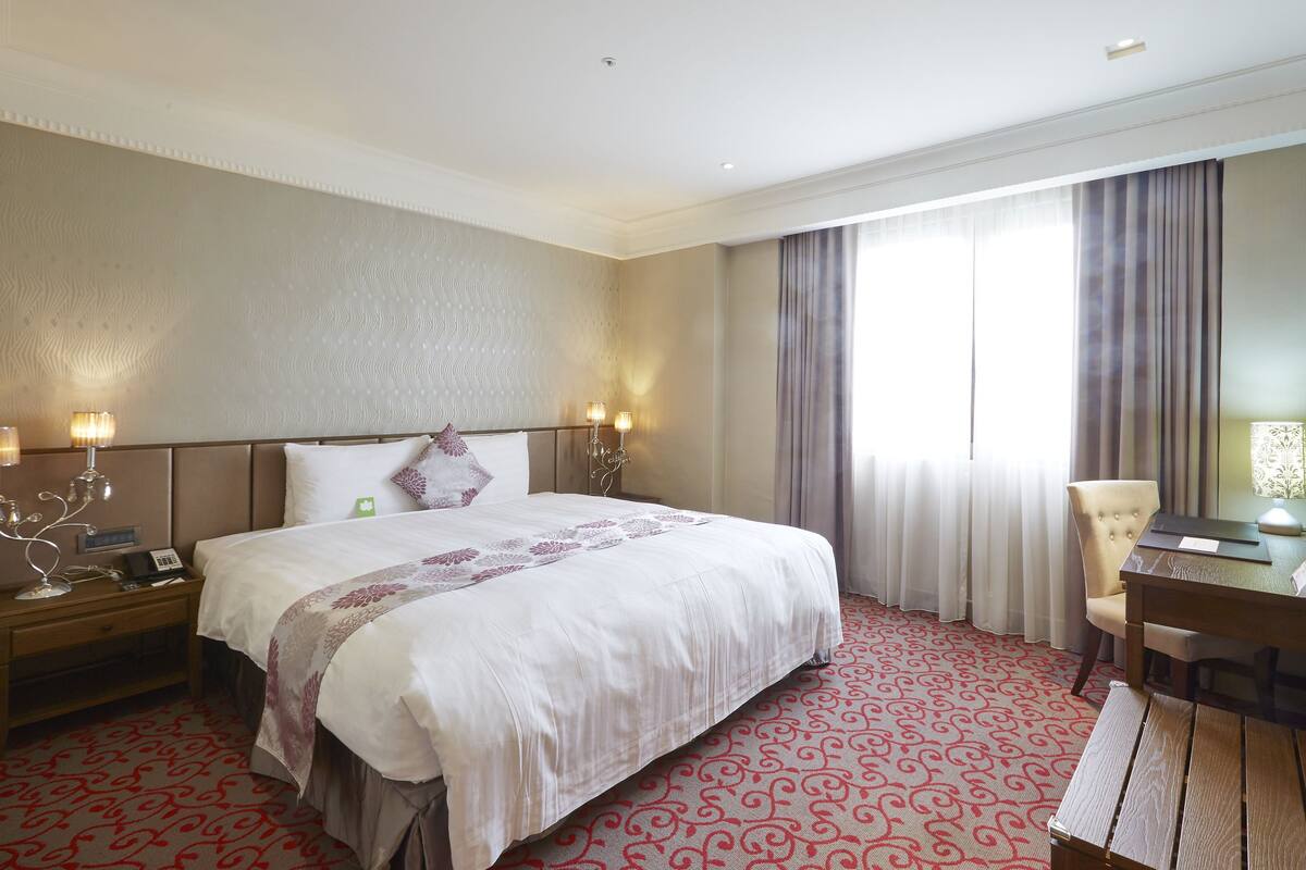 A hotel room with a large bed, bedside lamps, a desk, and a television.