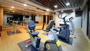 Un gimnasio con bicicletas estáticas y cintas de correr, suelos de madera y un espejo grande.
