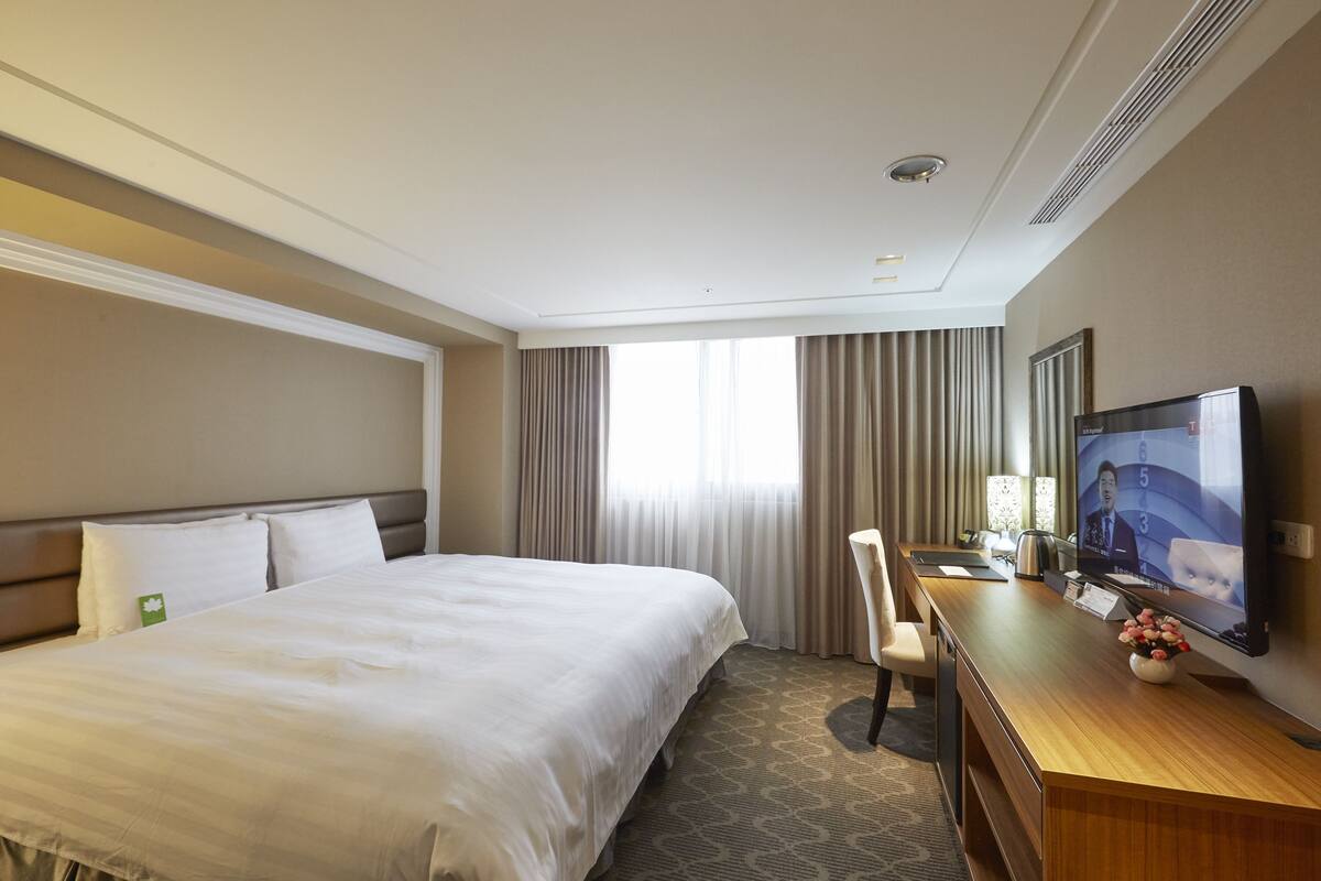 A hotel room with a large bed, a desk with a television, and a chair.