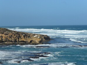 A coastal landscape with rocky cliffs and waves crashing against the shore. - Beachwalk Cottage (Blairgowrie)