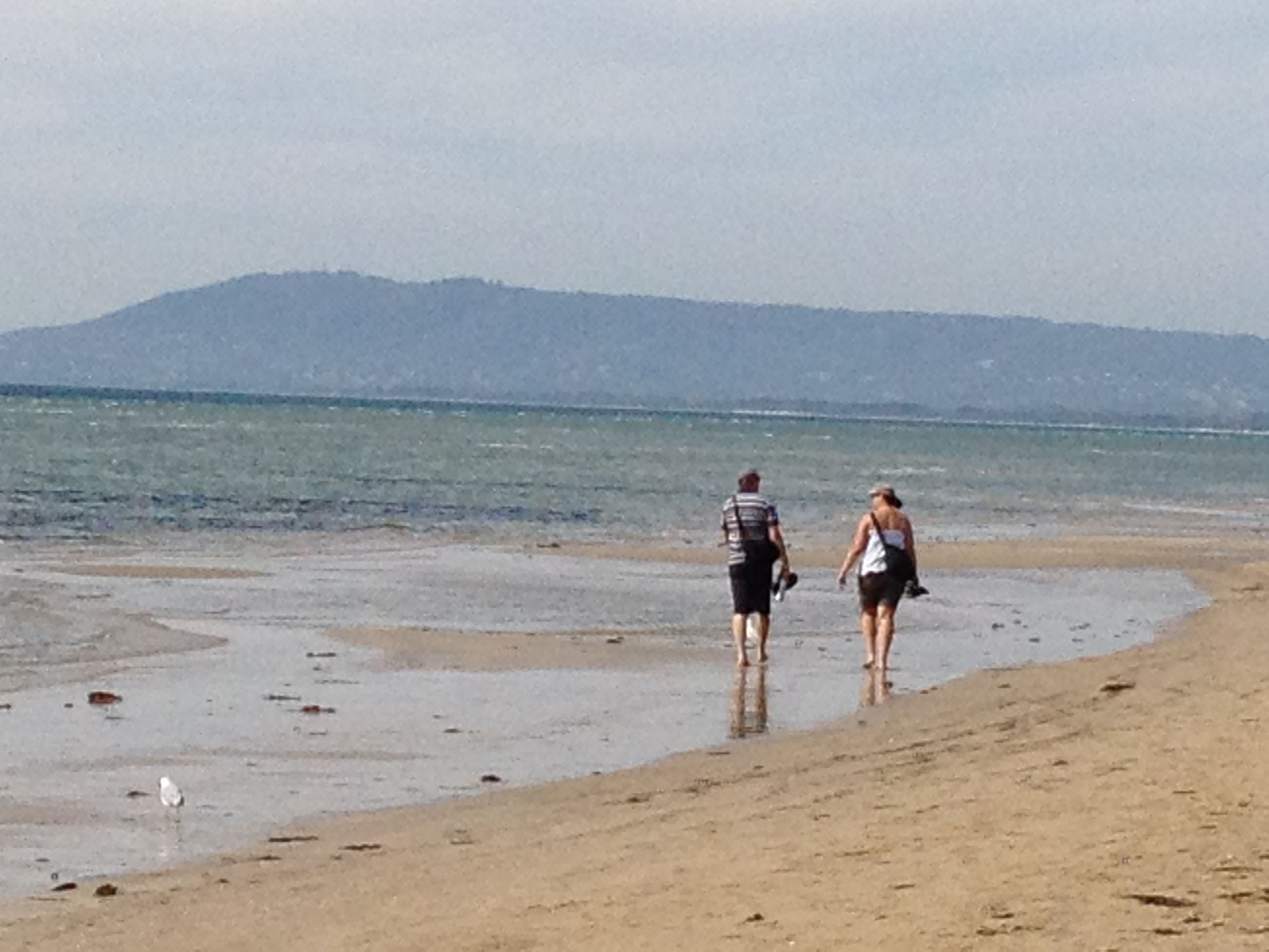 A beach with two people walking along the shore.