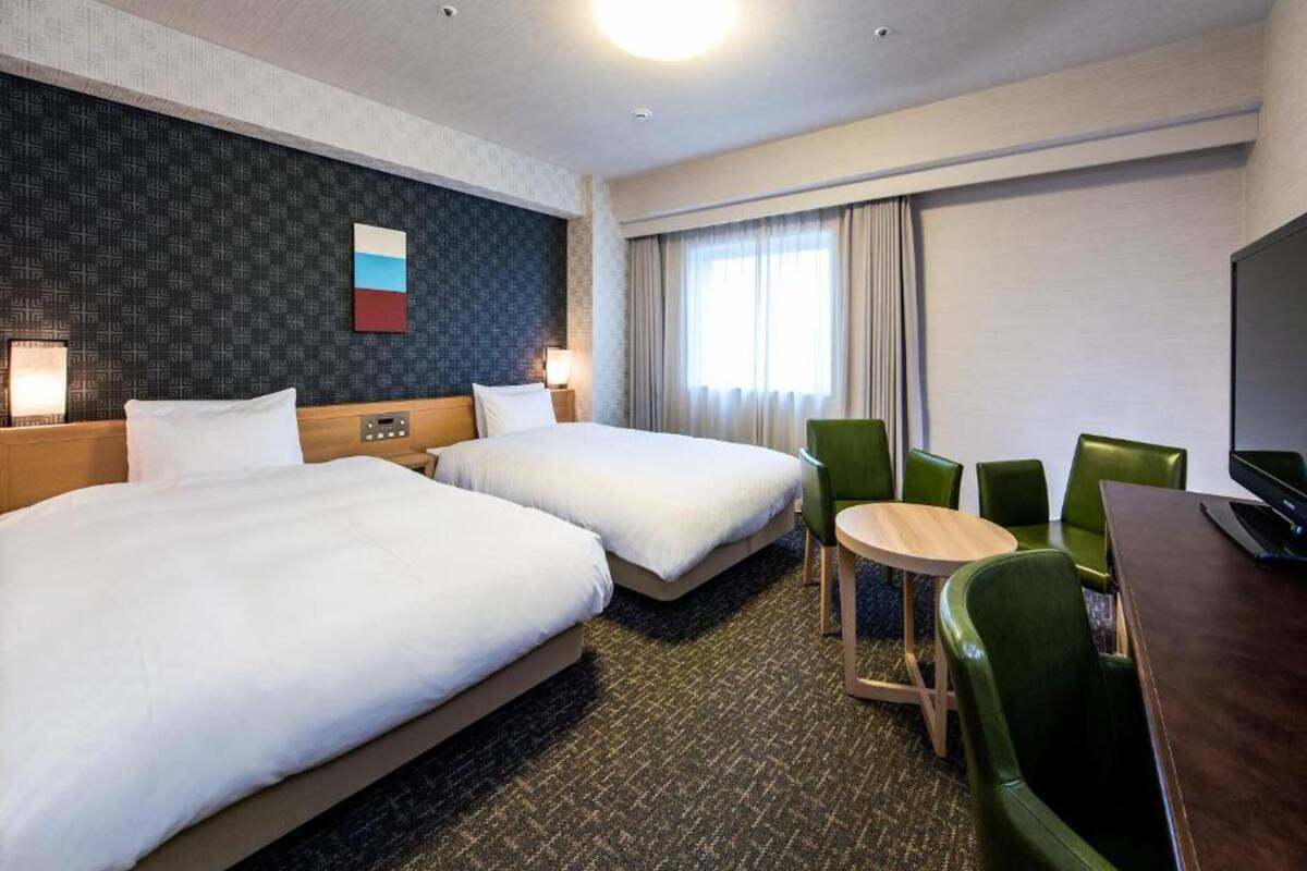Ein Hotelzimmer mit zwei Betten, einem kleinen runden Tisch und grünen Stühlen.