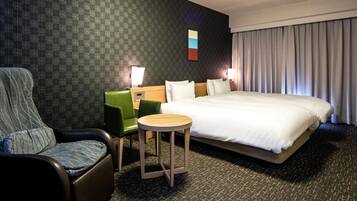 Una habitación de hotel con una cama grande, un sillón verde, una mesita redonda pequeña y un papel tapiz estampado.