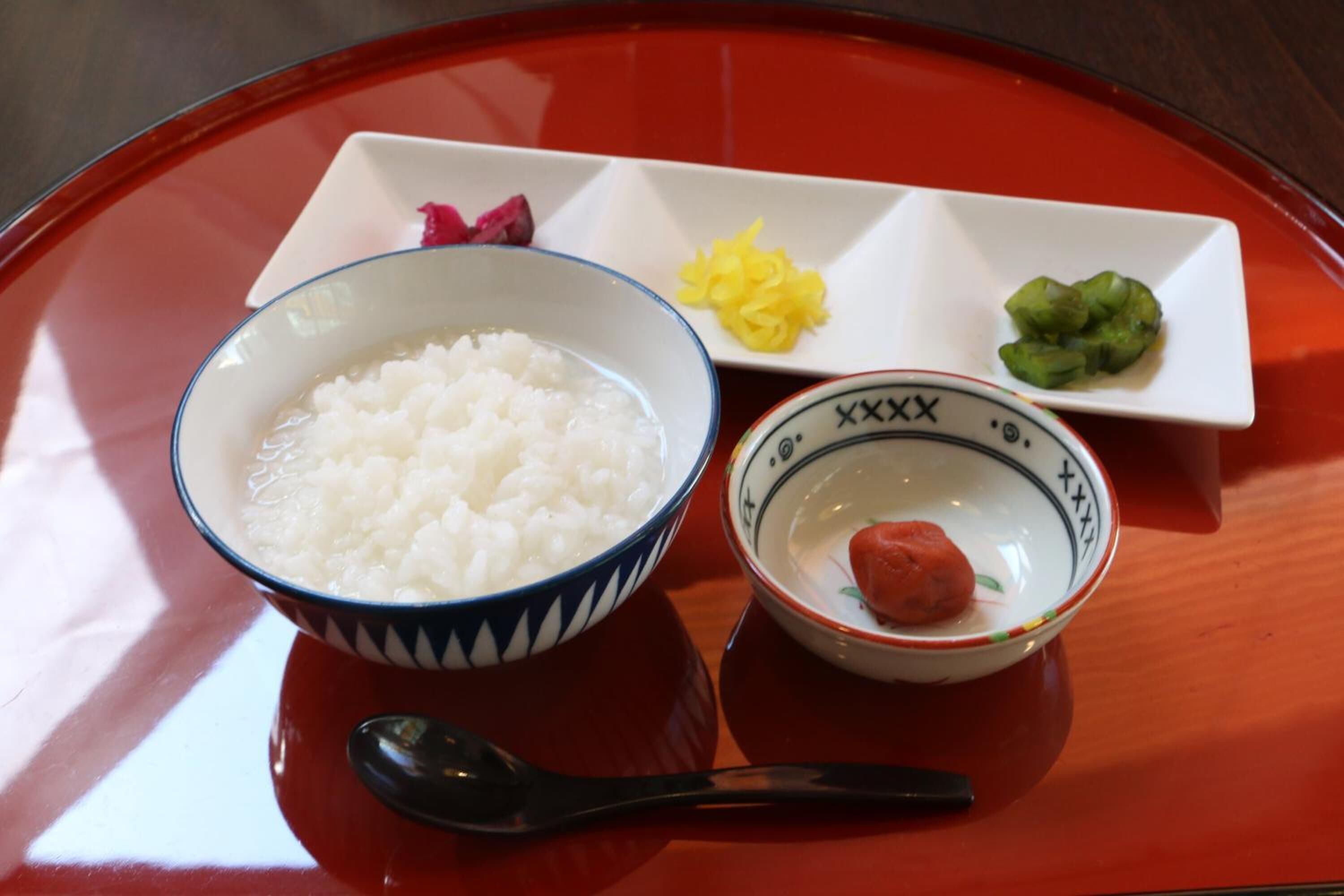 Una mesa con un tazón de arroz blanco, un plato pequeño con un elemento rojo, y dos platos pequeños con elementos amarillos y verdes.