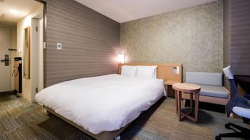 A hotel room with a large bed, a small round table, a sofa, and a desk with a chair.